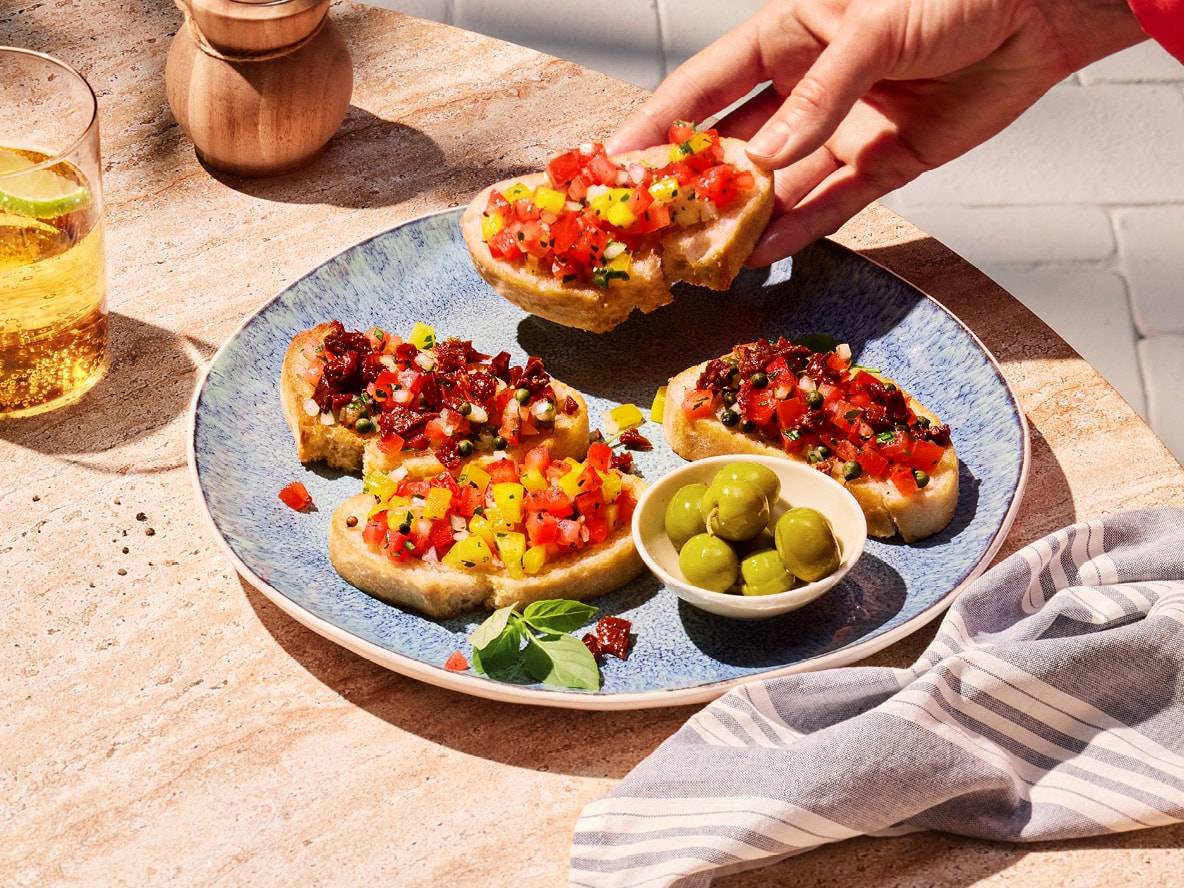 Bruschetta mit Tomaten und Paprika, Oliven und einem erfrischenden Getränk auf einem Steintisch.