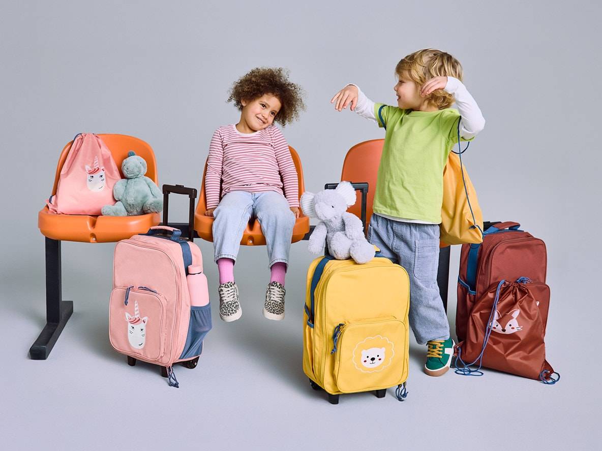 Zwei Kinder mit bunten Rollkoffern und Rucksäcken, bereit für die Reise.