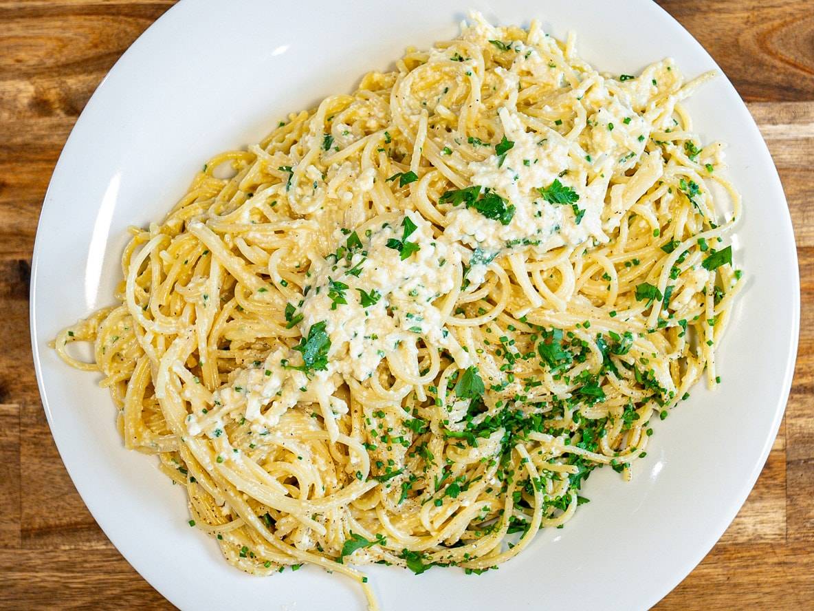 Cremige Spaghetti mit Käsesauce und frischen Kräutern auf einem weißen Teller.