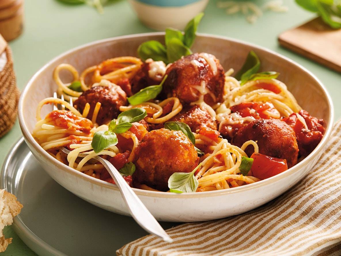 Spaghetti mit Fleischbällchen, Tomatensauce, Käse und Basilikum in einer Schale.
