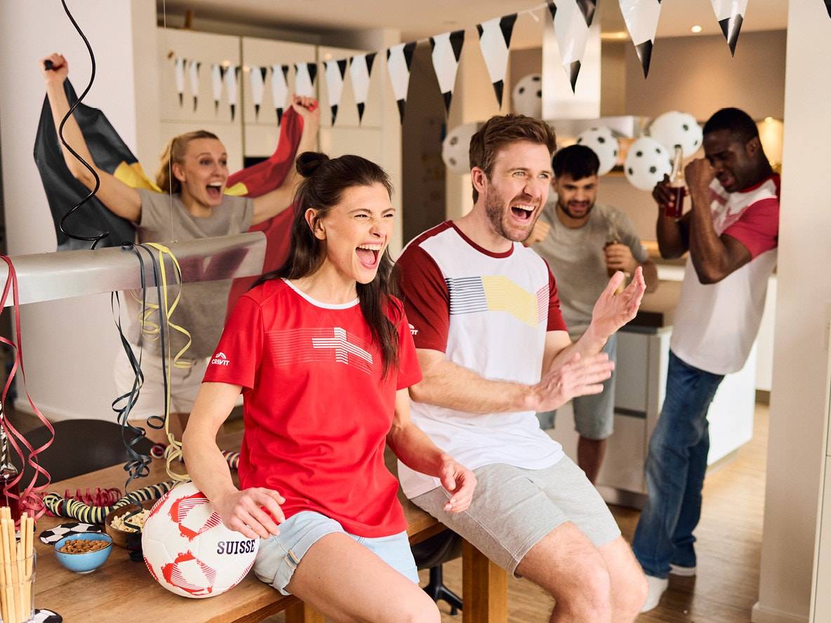 Amici festeggiano con maglie da calcio, bandiere e pallone da calcio con la scritta 'SUISSE'.