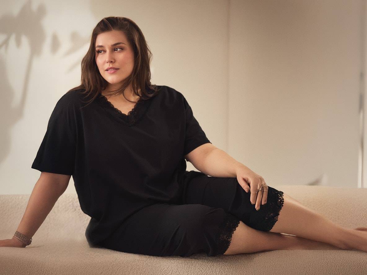 Donna in pigiama nero con pizzo, seduta su un divano chiaro.