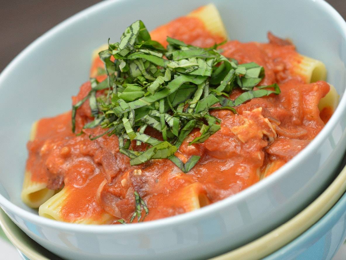 Rigatoni-Nudeln mit Tomatensauce und frischem Basilikum in einer hellblauen Schüssel.