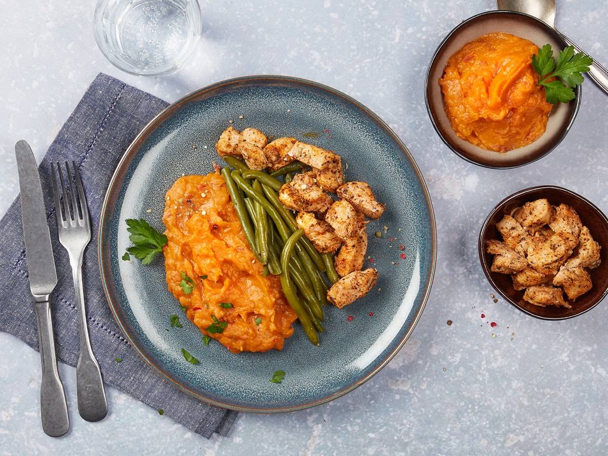 Pollo a cubetti con fagiolini e purè di patate dolci su un piatto blu.