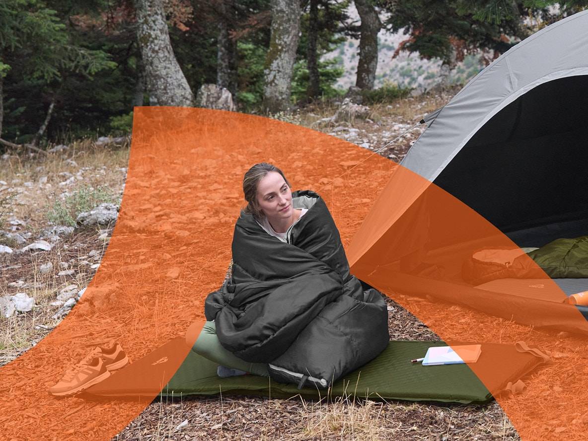 Frau im Schlafsack vor Zelt auf Isomatte beim Camping im Wald.