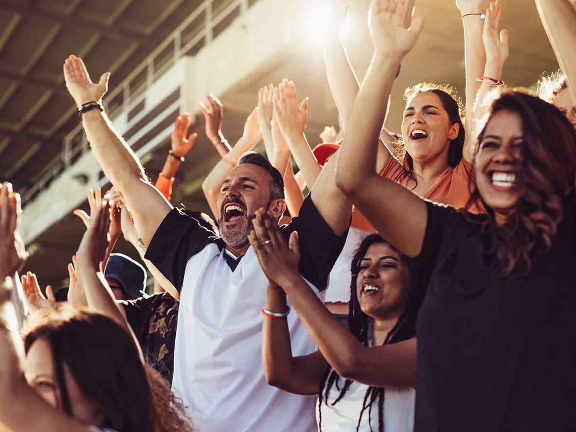 Fans enthousiastes dans un stade, applaudissant et célébrant les bras levés.