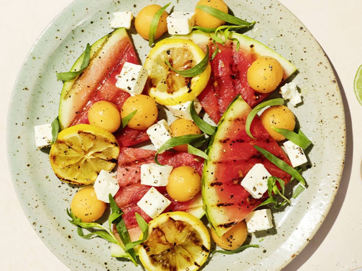 Pastèque grillée avec feta, billes de melon, citrons et herbes sur une assiette.