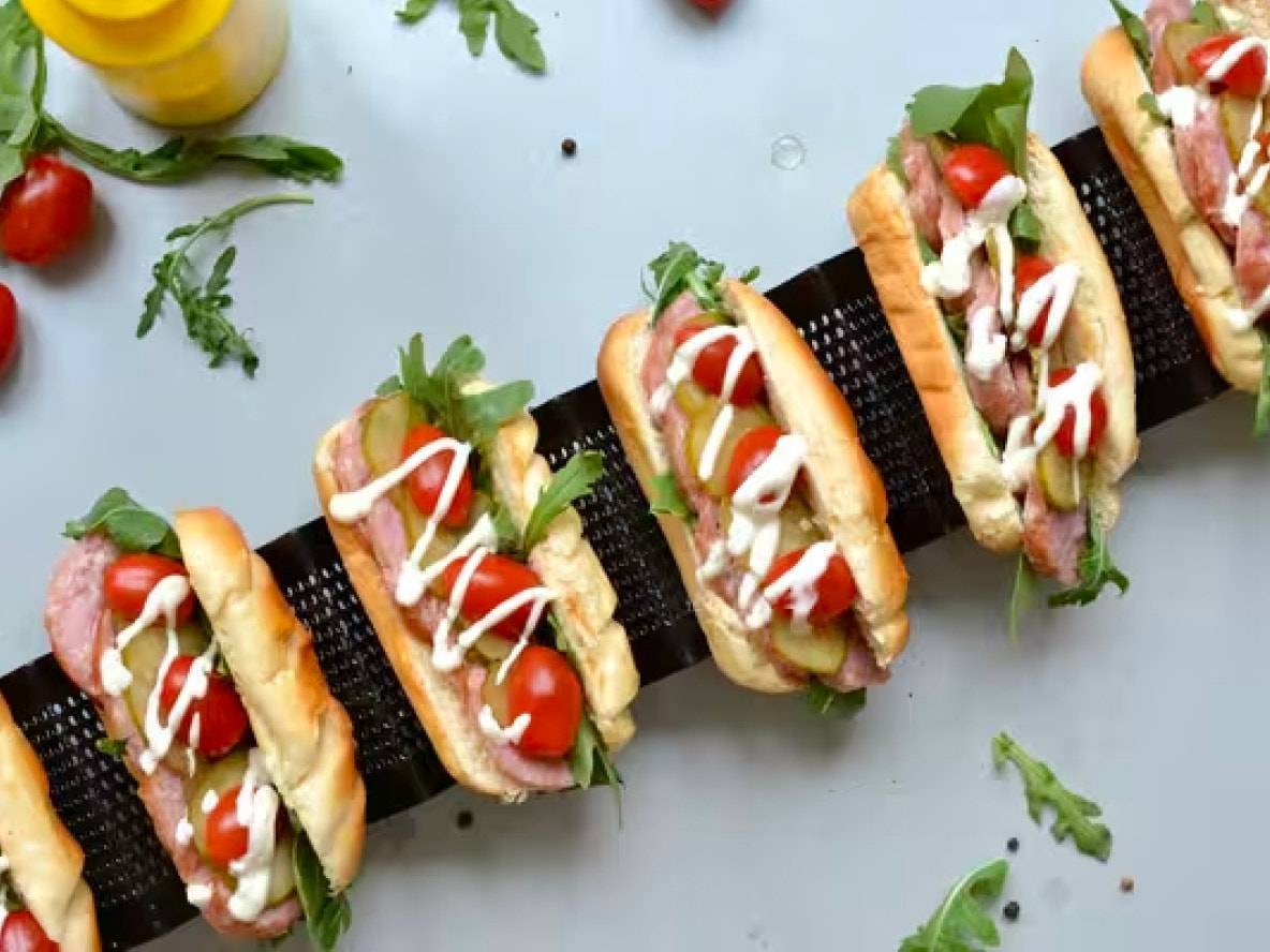 Reihe von Hotdogs mit Wurst, Rucola, Kirschtomaten, Gurken und Mayonnaise.