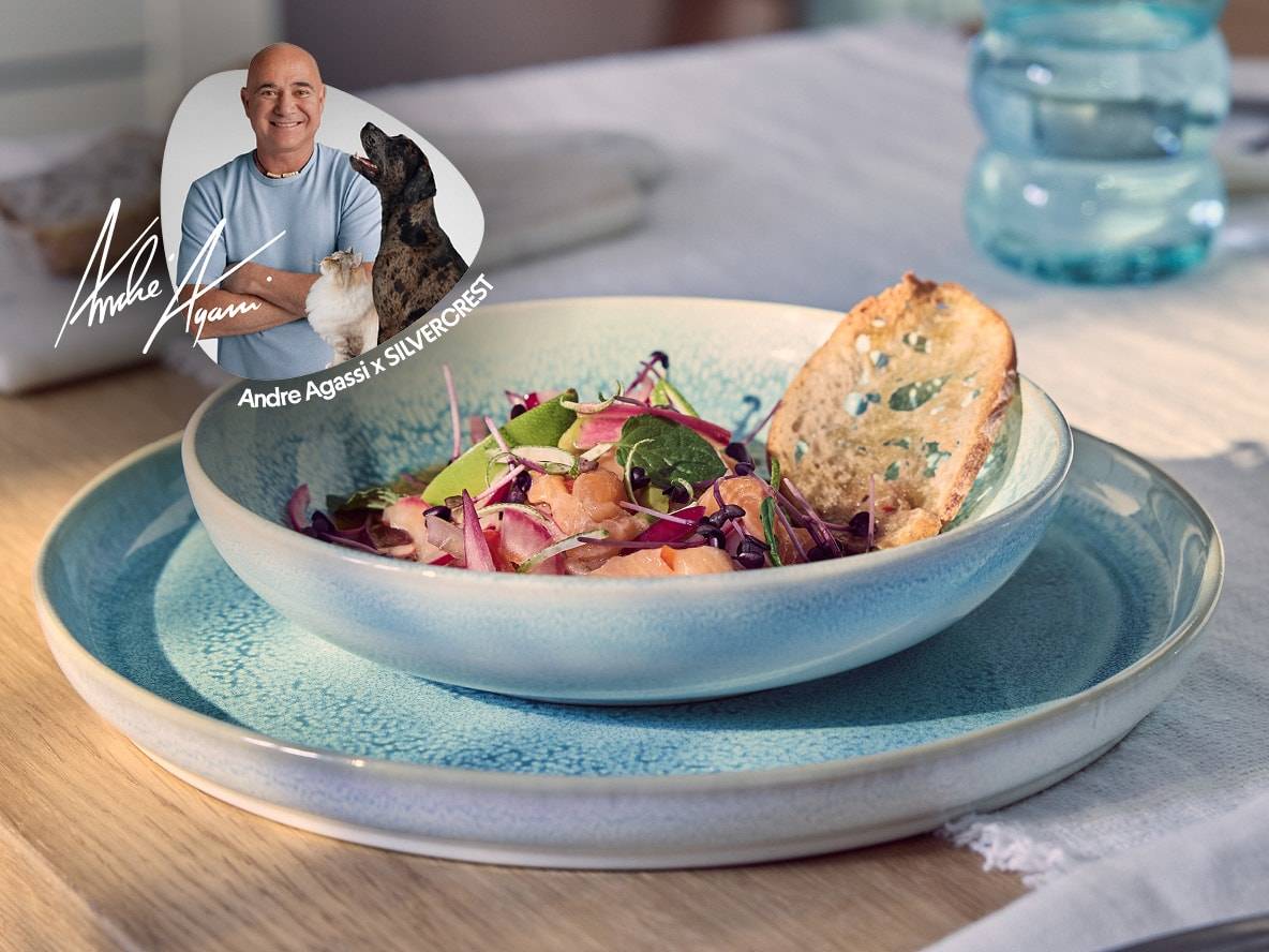 Una ciotola di insalata di salmone con pane tostato, su un piatto blu, con un ritratto di Andre Agassi.