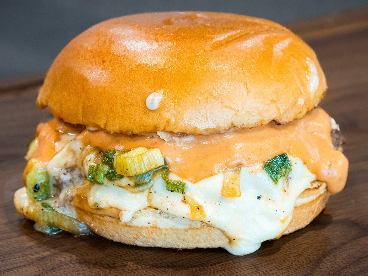 Hamburger con formaggio fuso, salsa cremosa e cipollotti su tagliere di legno.