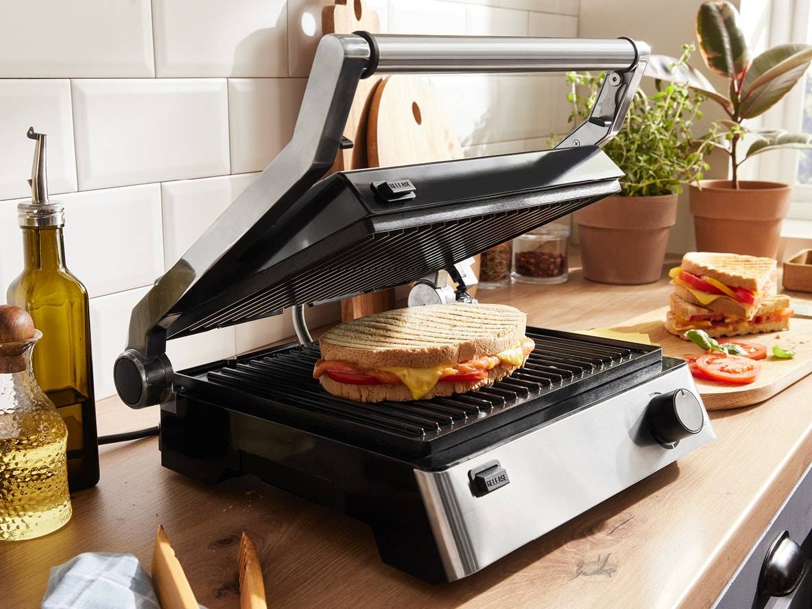 Ein elektrischer Sandwichtoaster bereitet ein gegrilltes Sandwich auf einer Küchenoberfläche zu.