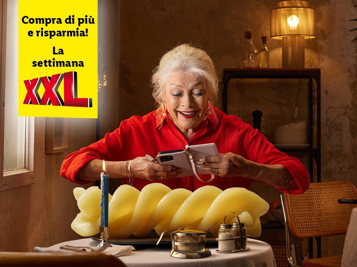 Una donna anziana usa il suo cellulare accanto a una porzione gigante di pasta XXL.