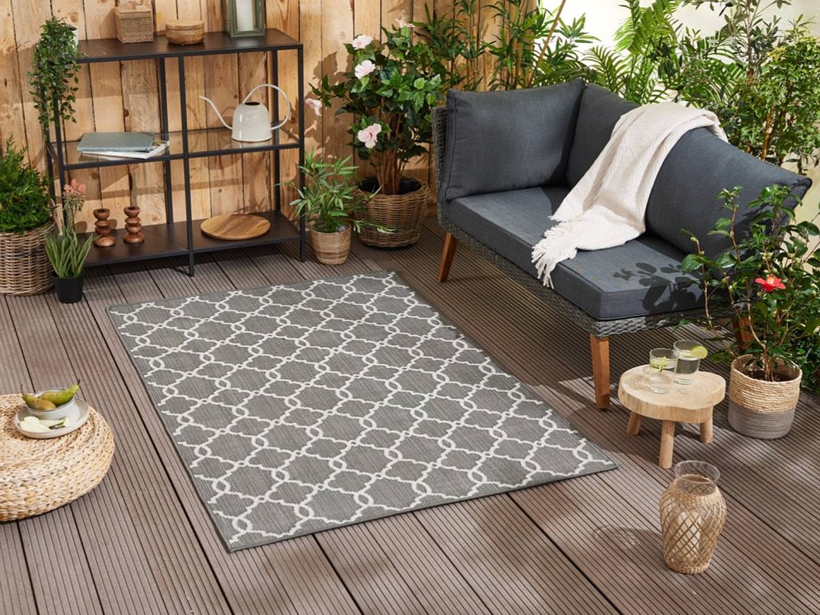 Tappeto da giardino grigio chiaro con motivo geometrico su un patio con mobili da giardino.
