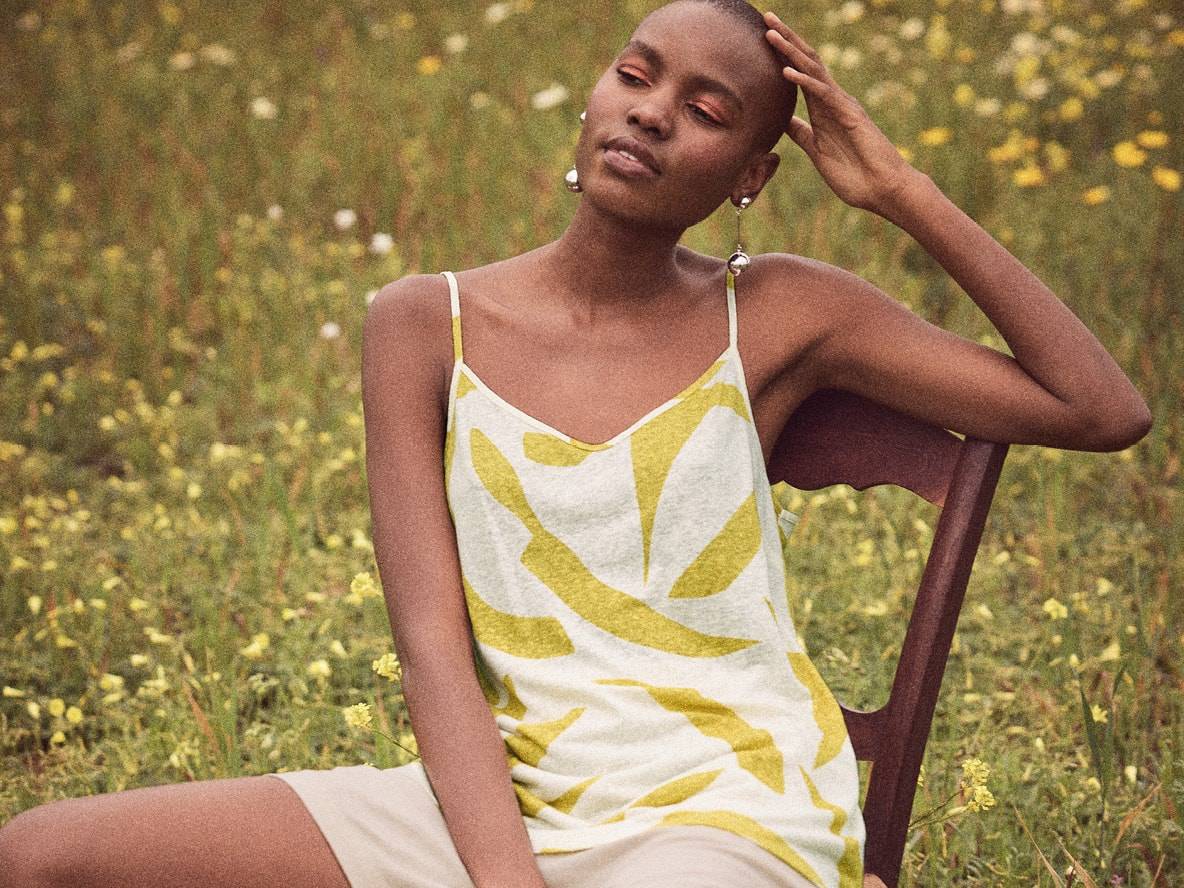 Una donna indossa una camicetta senza maniche con stampa giallo chiaro e una gonna corta beige in un campo fiorito.