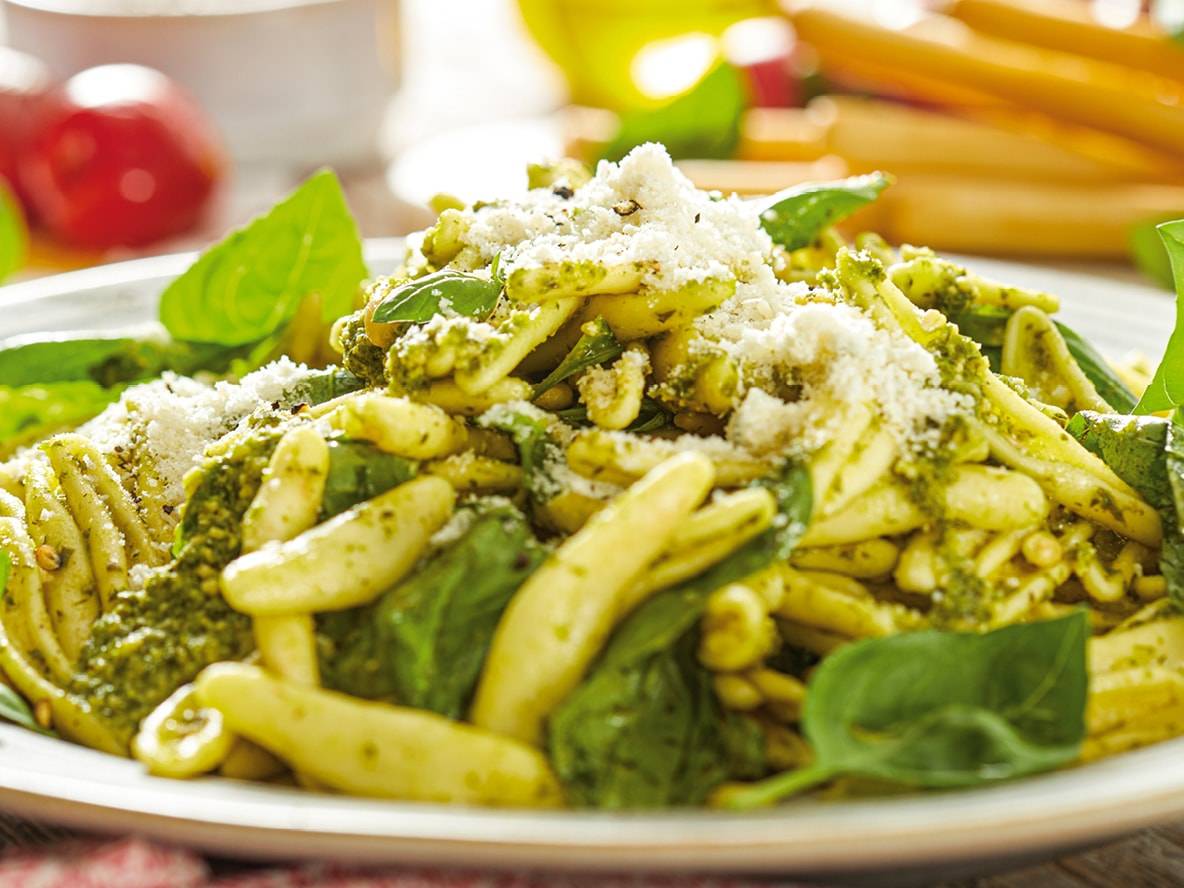 Pesto-Nudeln mit geriebenem Parmesan und frischen Basilikumblättern.