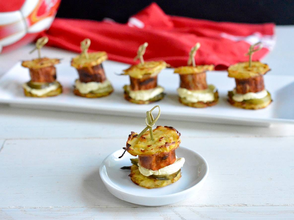 Kartoffel-Mini-Burger mit Wurst, Gurken und Mayonnaise auf einem weißen Teller.