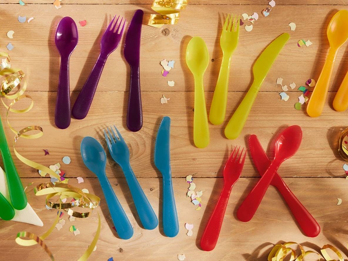 Buntes Partybesteck aus Plastik auf einem Holztisch mit Konfetti.