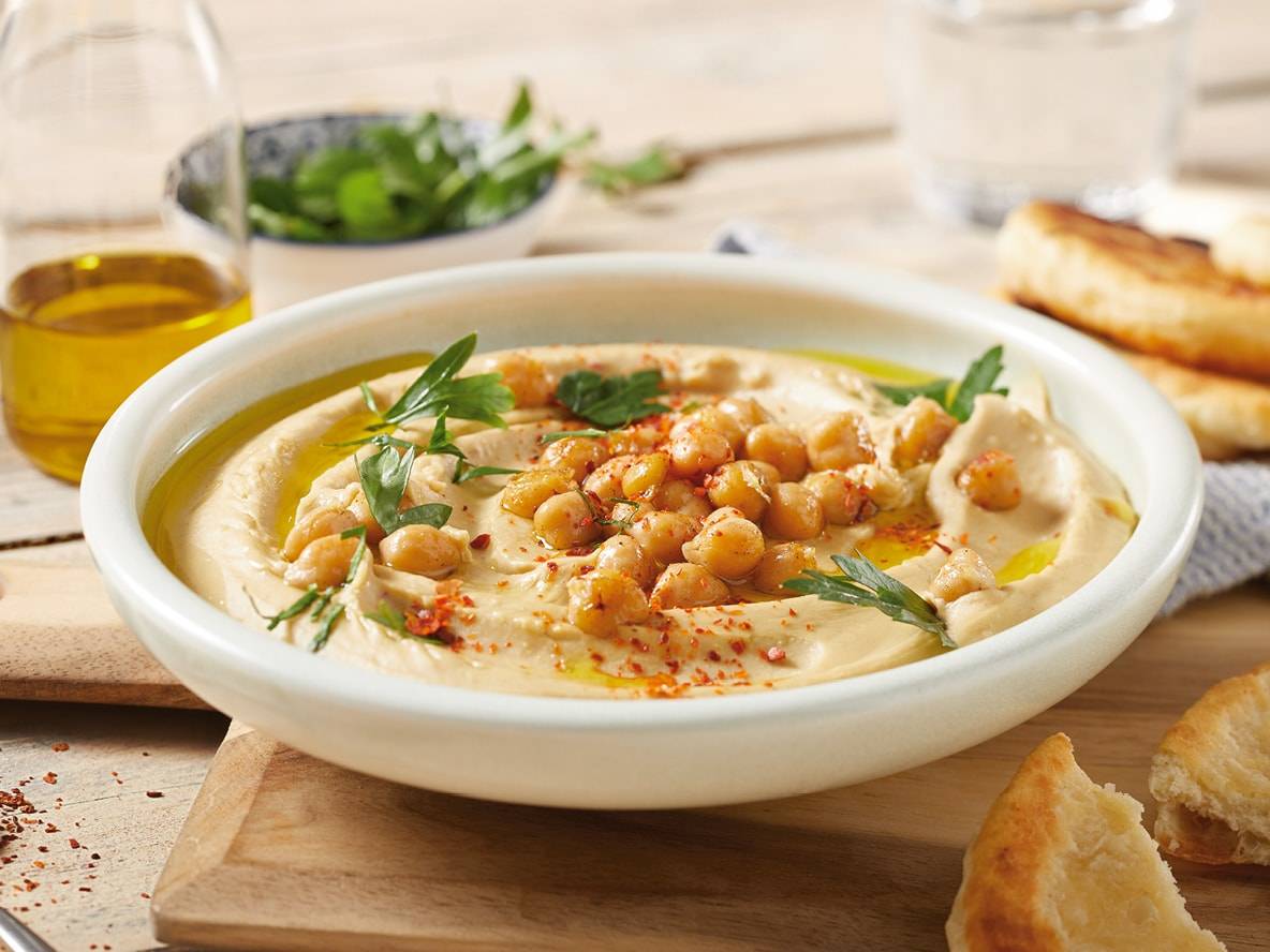 Eine Schale Hummus, garniert mit Kichererbsen, Petersilie und Paprika, serviert mit Brot und Olivenöl.