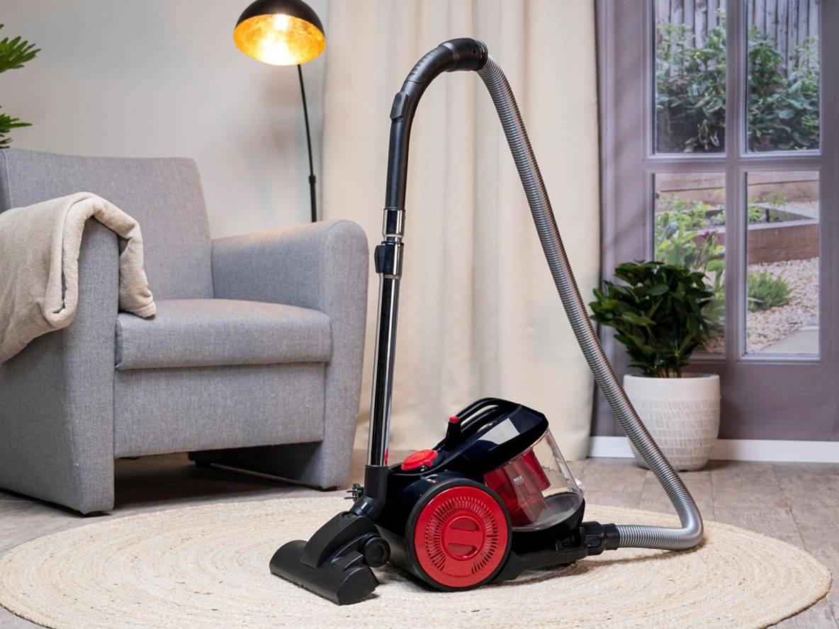 Schwarz-roter Staubsauger auf einem runden Teppich in einem Wohnzimmer.