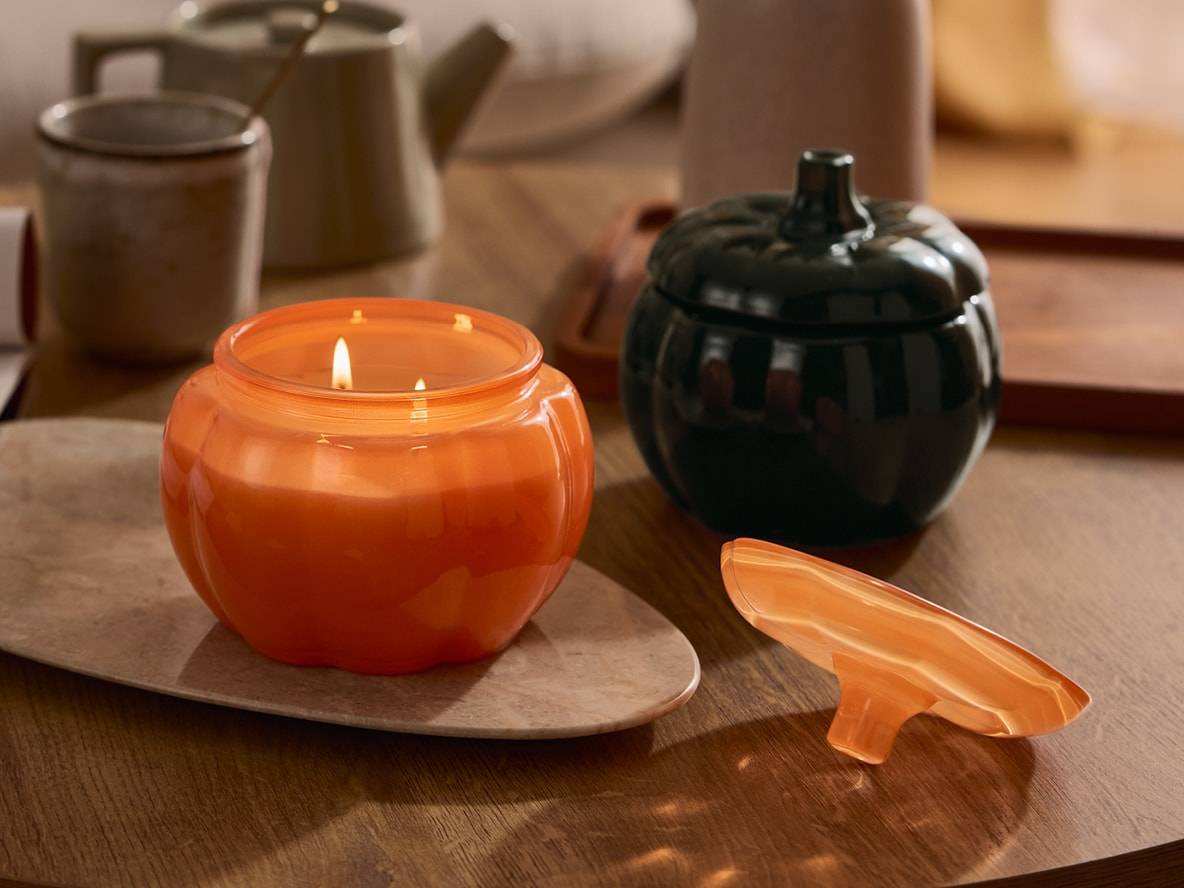 Orangefarbene und schwarze Kürbiskerzen auf einem Holztisch.