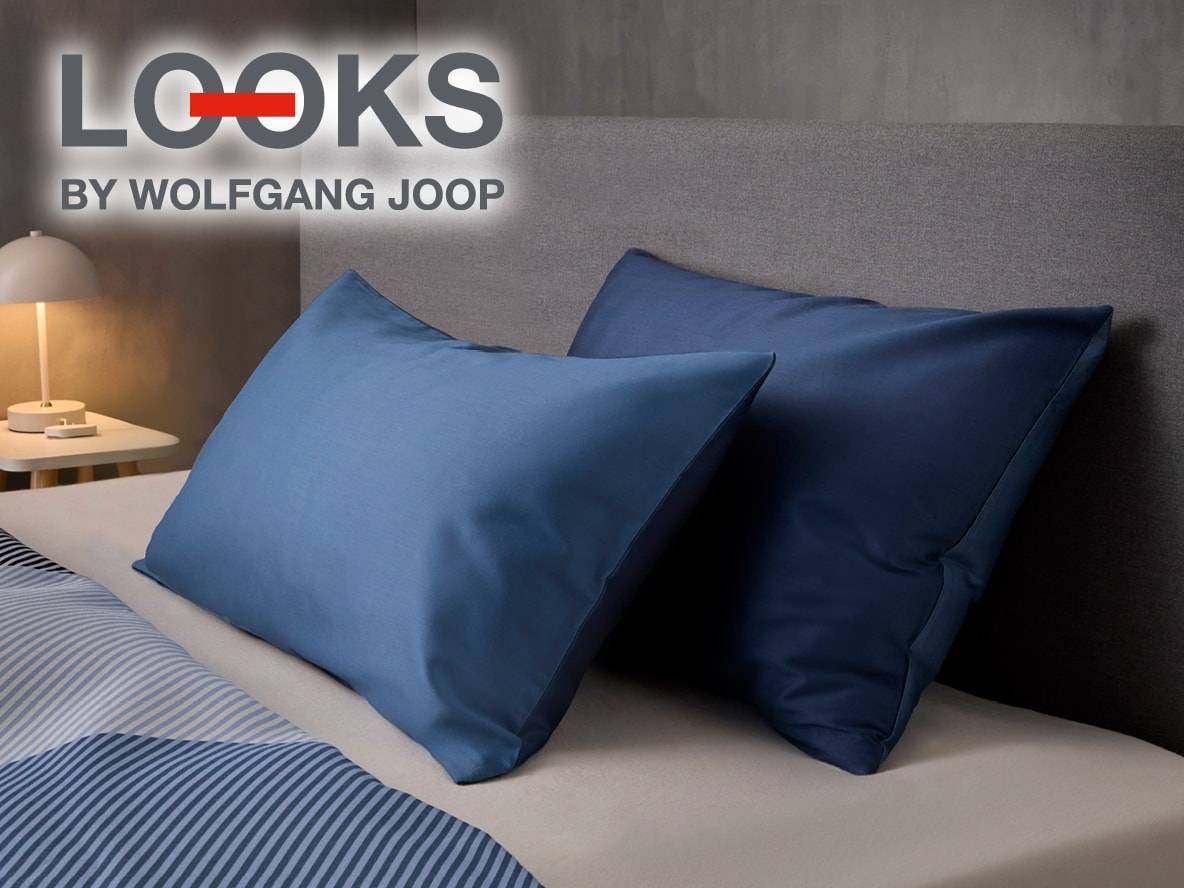 Ein Bett mit blauen Kissen und gestreifter Bettwäsche, mit dem Logo 'LOOKS BY WOLFGANG JOOP'.