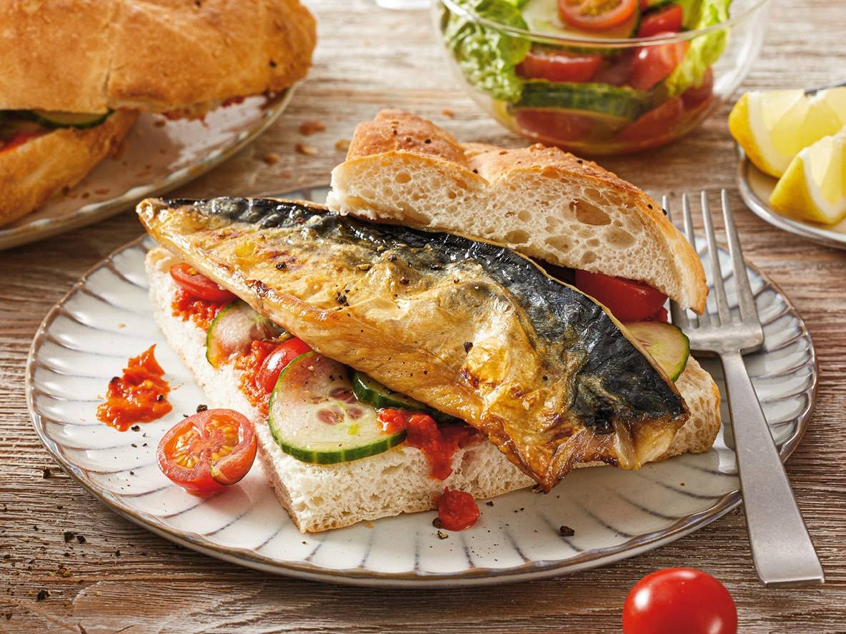 Sandwich mit gegrillter Makrele, Tomaten und Gurken, dazu Salat und Zitrone.