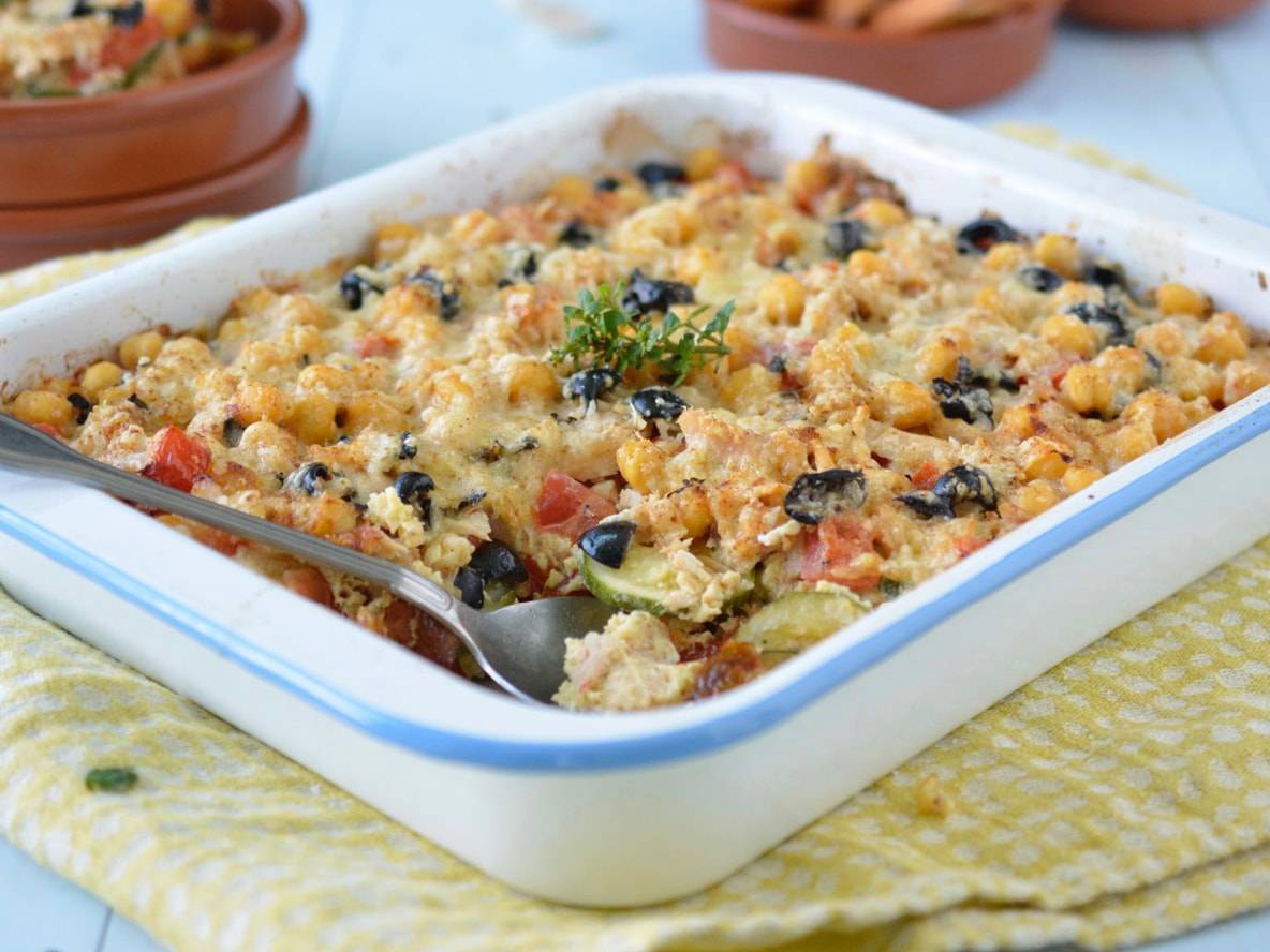 Un plat de gratin de pois chiches, olives et légumes avec une cuillère.