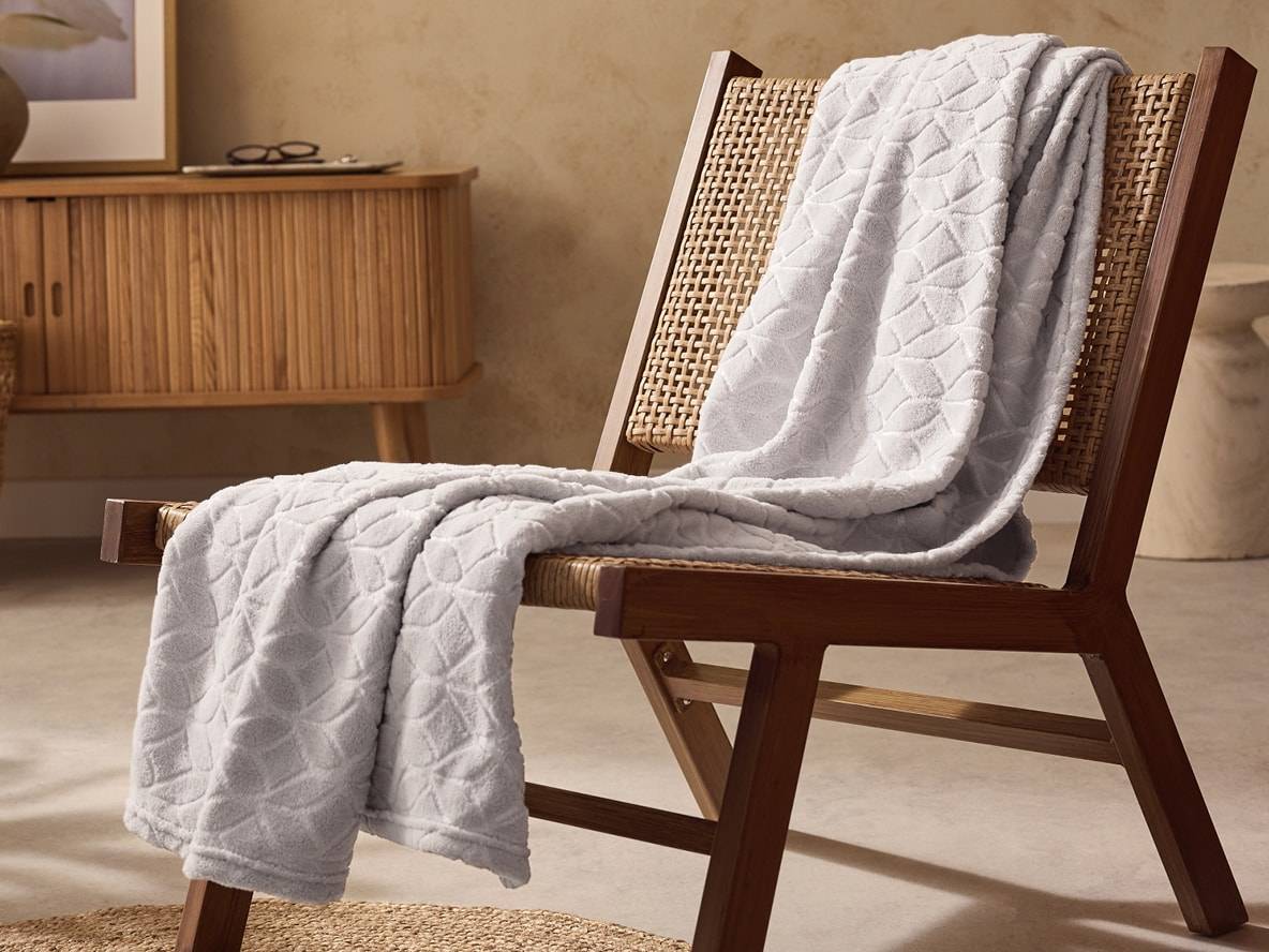 Un plaid gris à motifs géométriques drapé sur une chaise en bois et rotin.