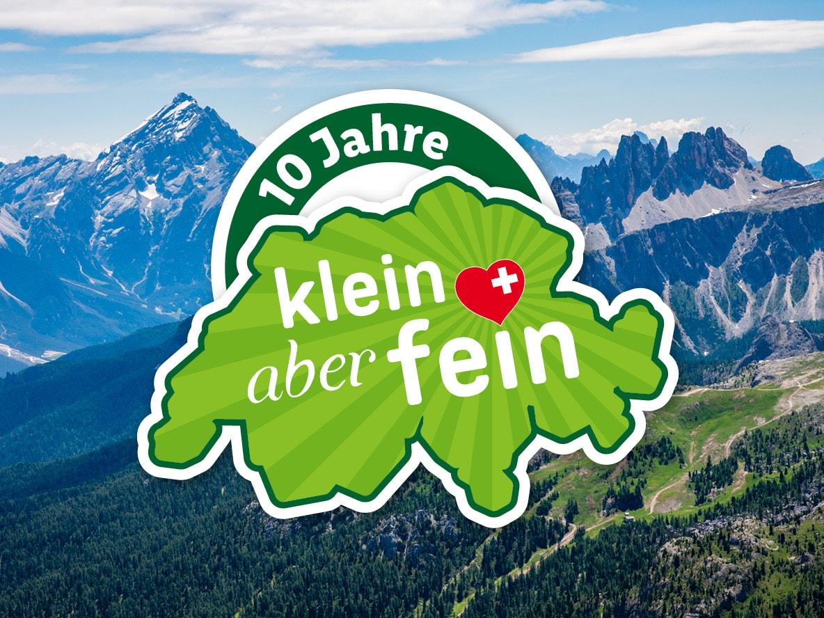 Logo '10 Jahre klein aber fein' in Form der Schweiz vor einer Bergkulisse.