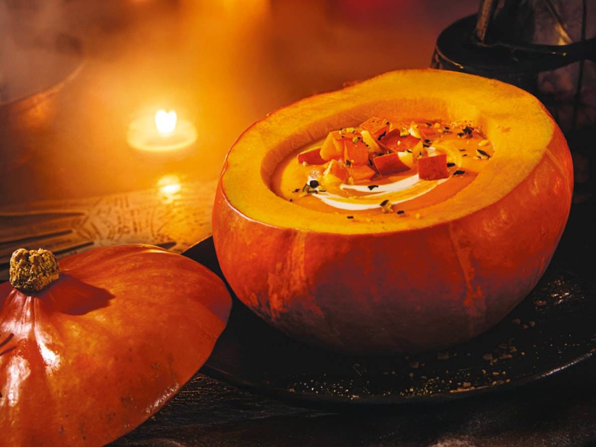 Zuppa di zucca servita in una zucca scavata, con una candela sullo sfondo