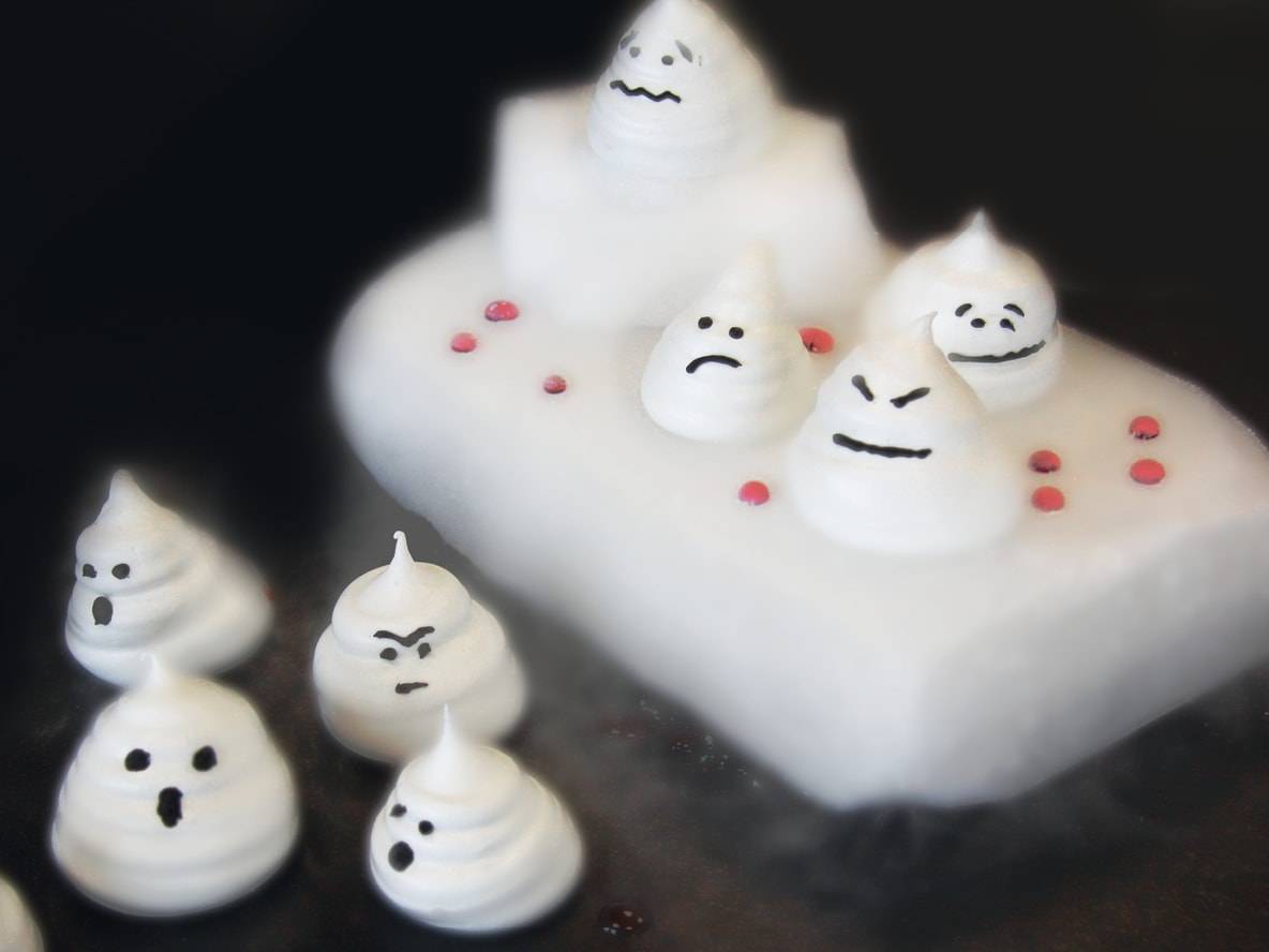 Halloween-Baiser-Geister auf einem weißen Kuchen mit roten Streuseln.