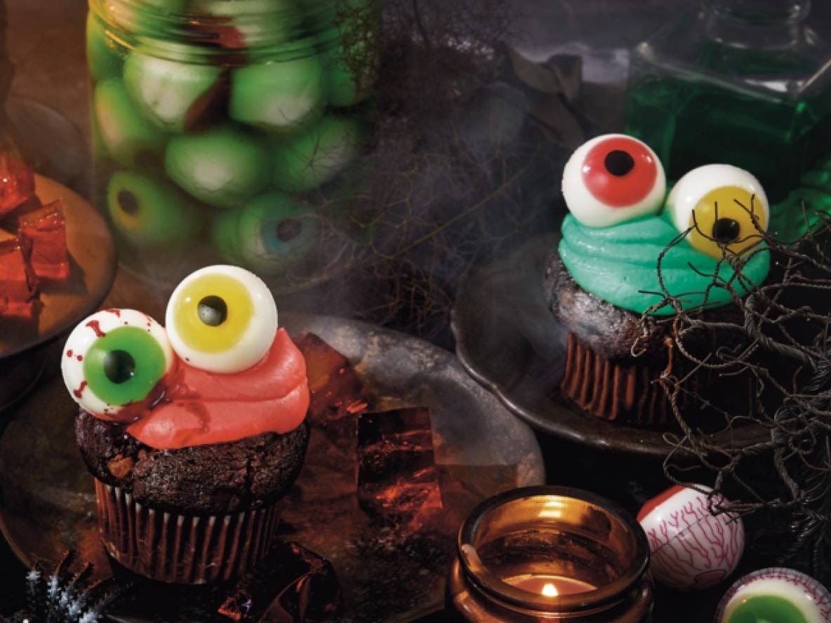 Halloween-Cupcakes mit Augen, ein Glas mit schwimmenden Augen und Süßigkeiten.