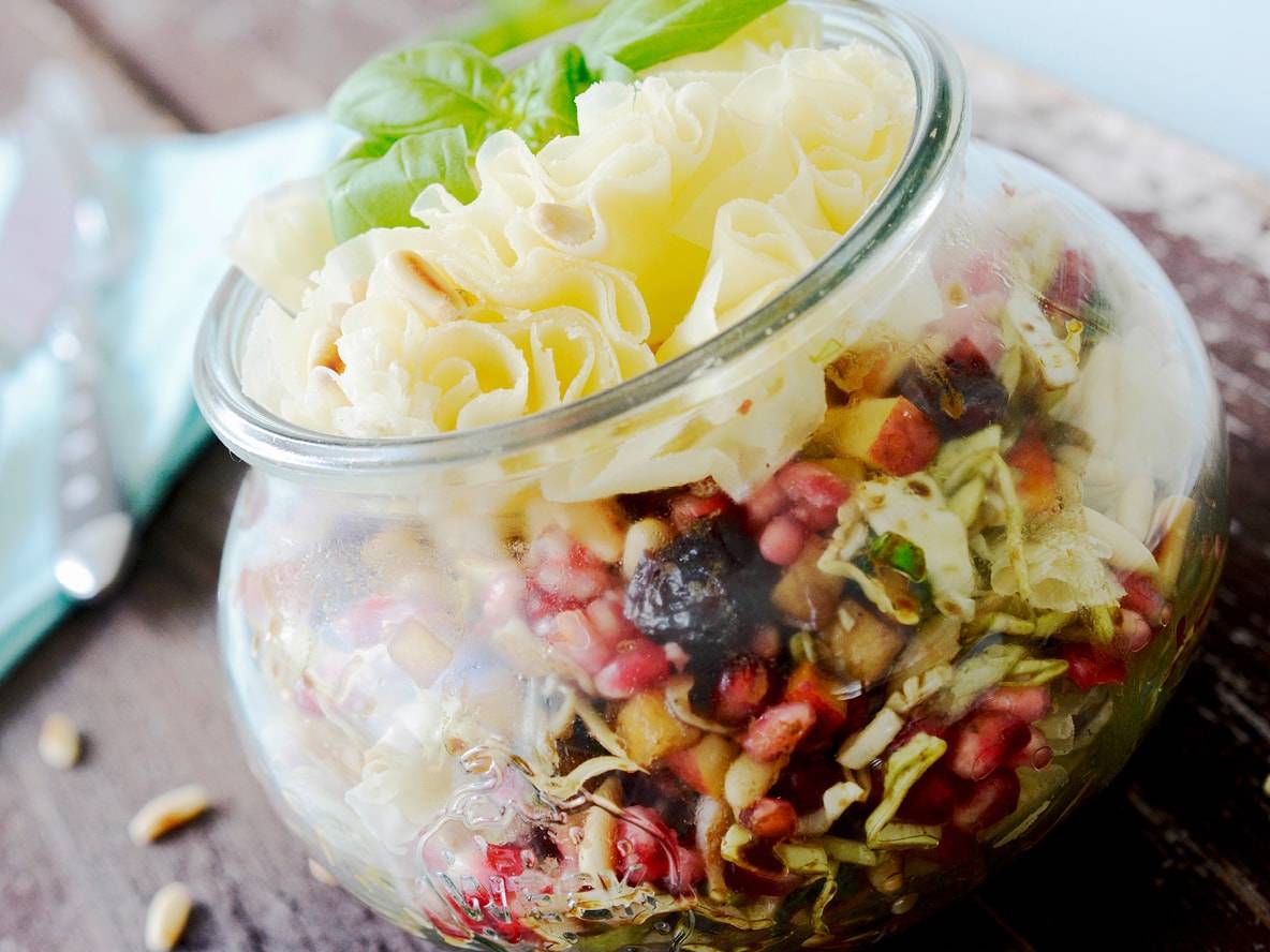 Glasgefäß mit Salat, Granatapfel, Kohl und Käsespänen, garniert mit Basilikum.
