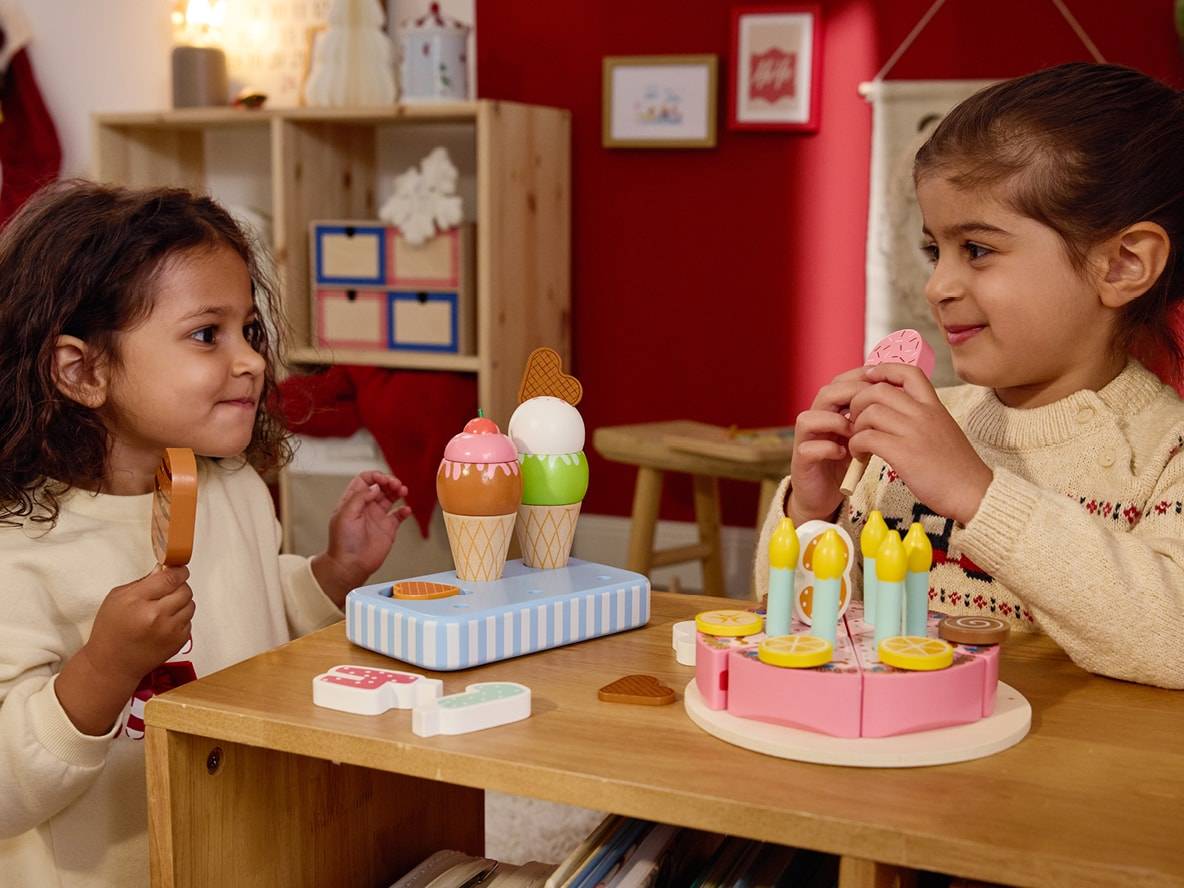 Zwei kleine Mädchen spielen mit einem Eiscreme-Set und einem Holzkuchen.