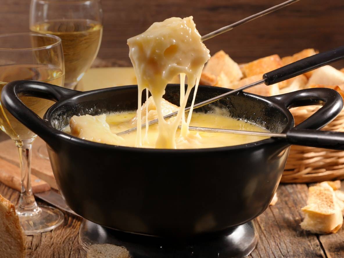 Heißes Käsefondue mit Brot und Weißwein auf einem Holztisch.