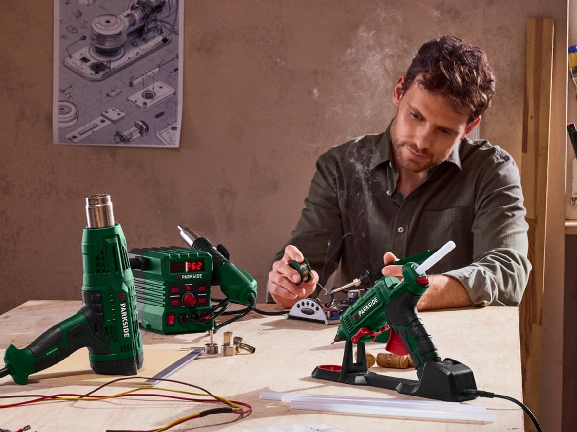 Mann lötet mit Parkside-Werkzeugen, darunter eine Heißluftpistole und eine Heißklebepistole.