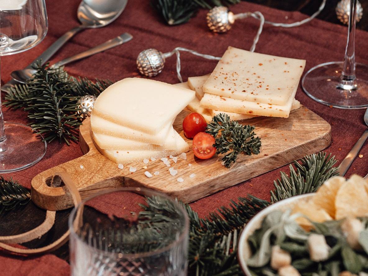 Käsescheiben auf Holzbrett mit Kirschtomaten und Weihnachtsdekoration.