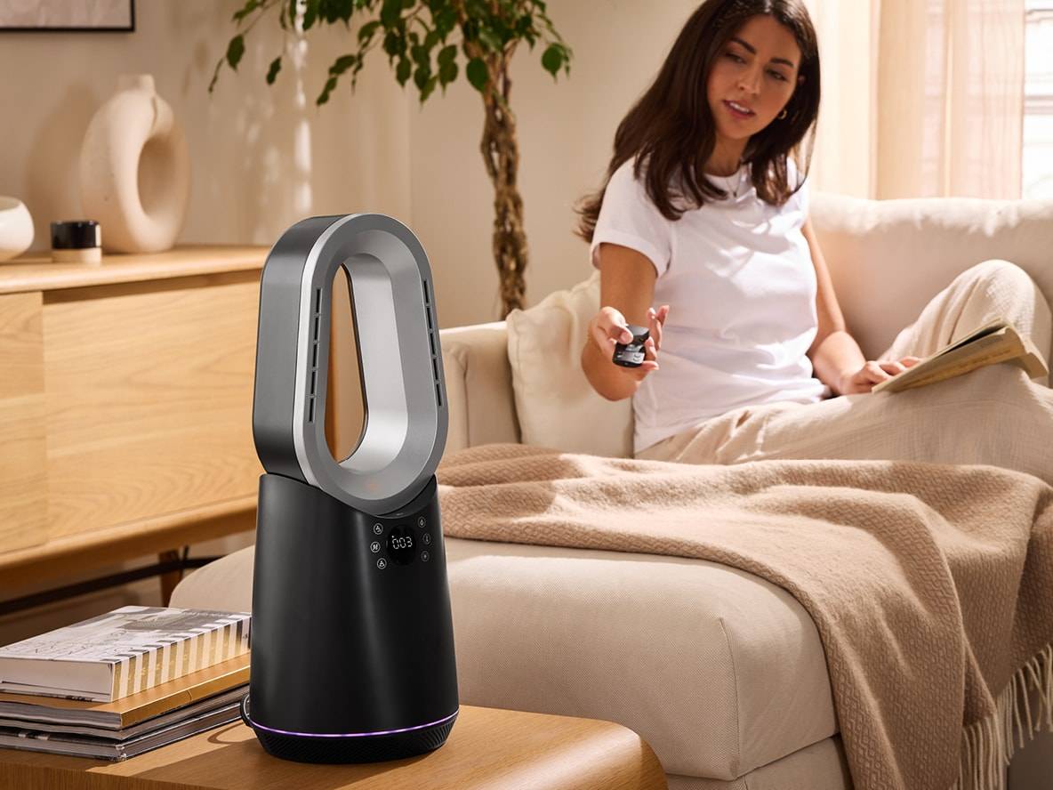 Eine Frau bedient einen schwarz-grauen Luftreiniger mit einer Fernbedienung in einem modernen Wohnzimmer.