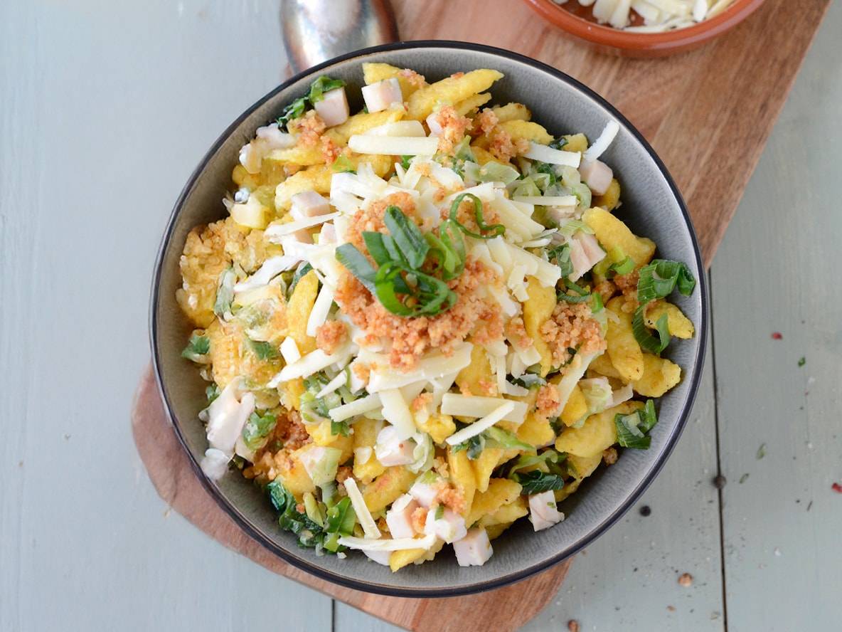 Un bol de spätzle au fromage, jambon, oignons verts et chapelure.