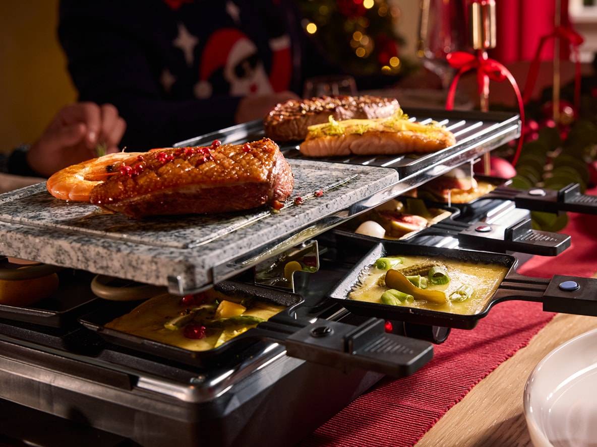 Raclette mit Fleisch, Fisch, Garnelen und Pfännchen mit geschmolzenem Käse.