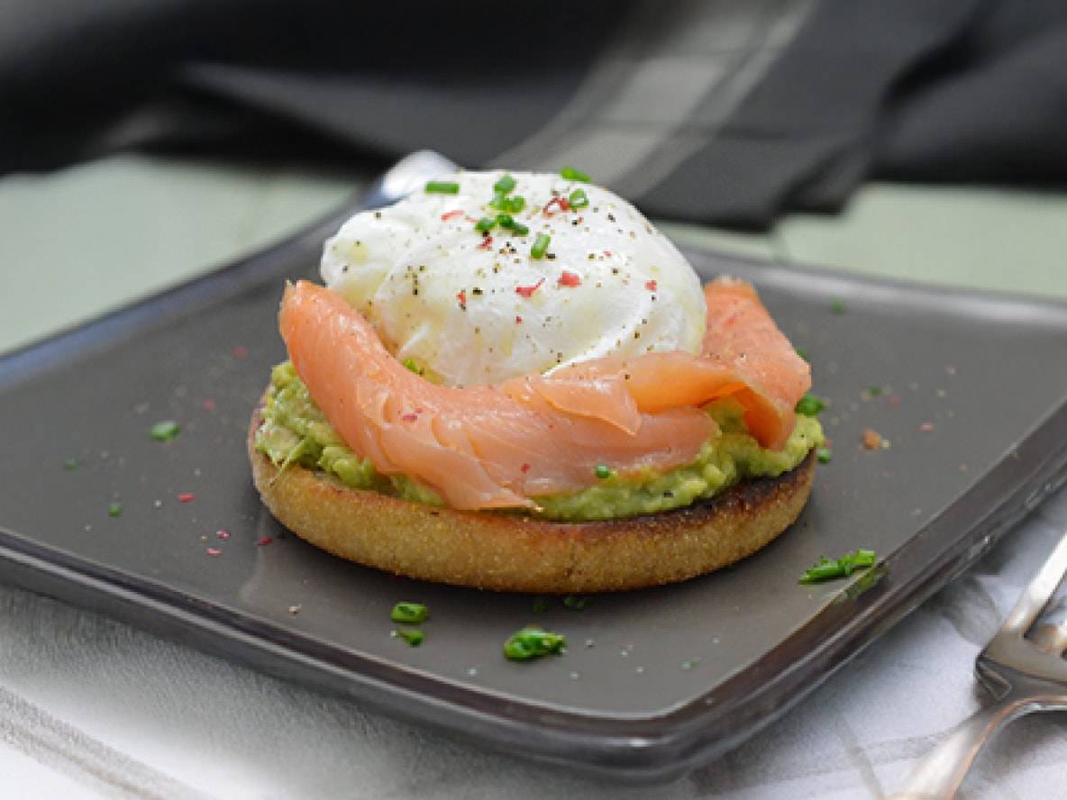 Englischer Muffin mit Avocado, Räucherlachs und pochiertem Ei, garniert mit Schnittlauch und rosa Pfeffer.