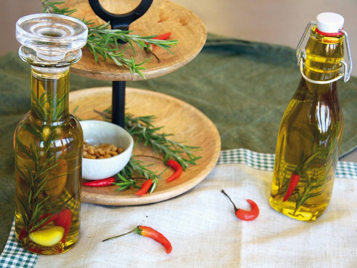 Zwei Flaschen Olivenöl, infundiert mit Rosmarin, Chilischoten und Knoblauch, auf einem Tisch.