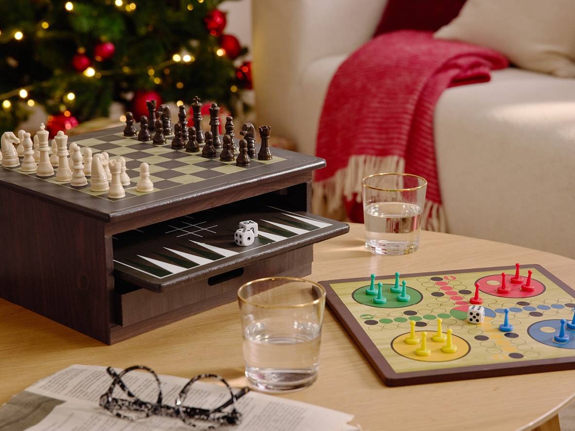 Schach- und Backgammon-Holzspiel mit einem Ludo-Spiel auf einem Couchtisch, neben einem Weihnachtsbaum.