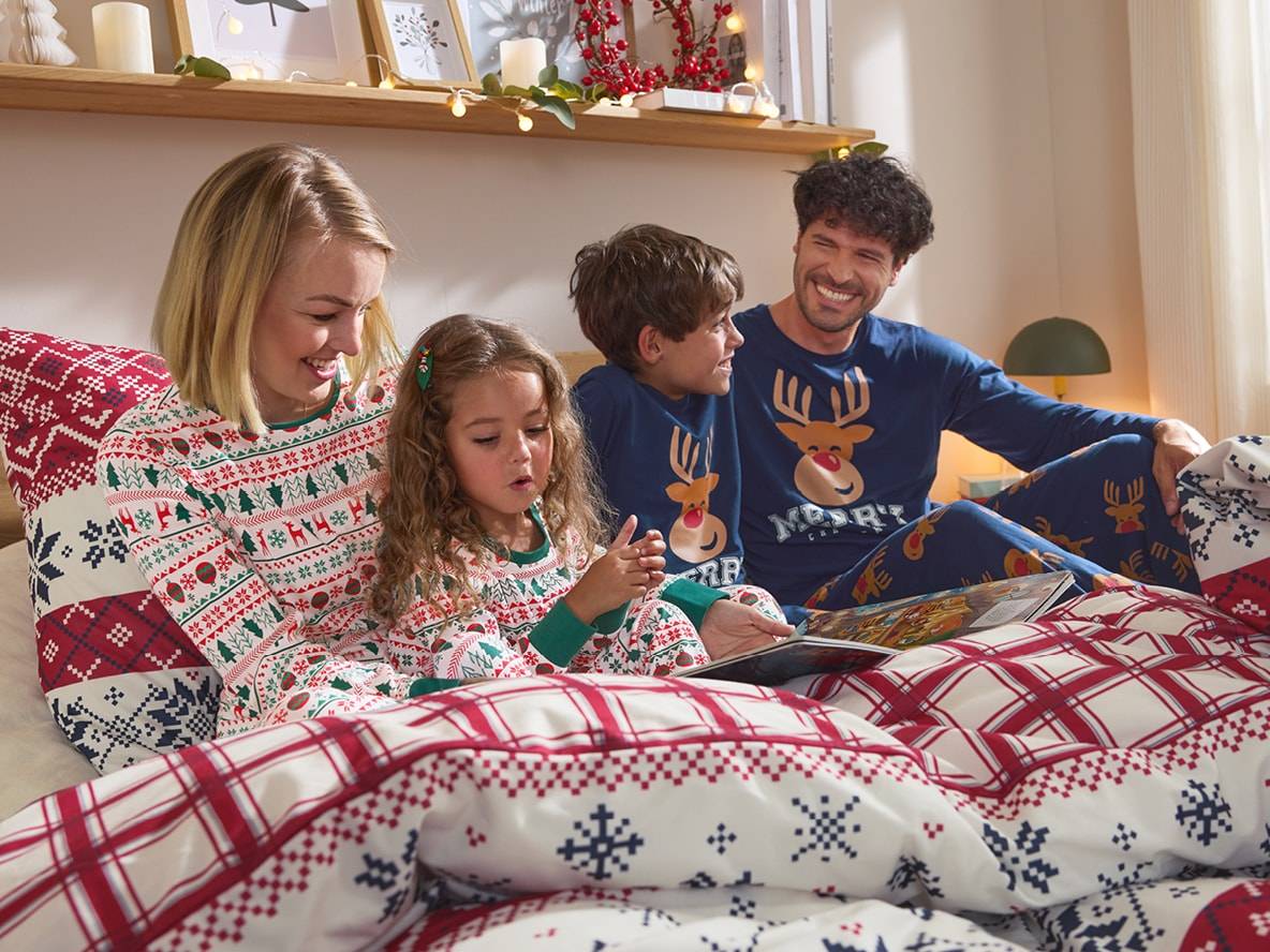 Familie in passenden Weihnachtspyjamas liest ein Buch im Bett.