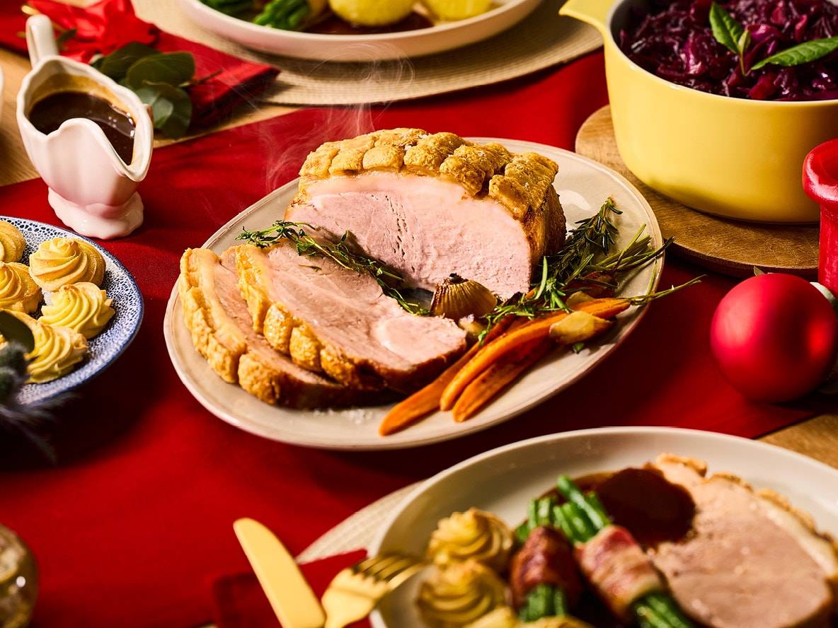Saftiger Schweinebraten mit Gemüse und Soße auf einem roten Weihnachtstisch.