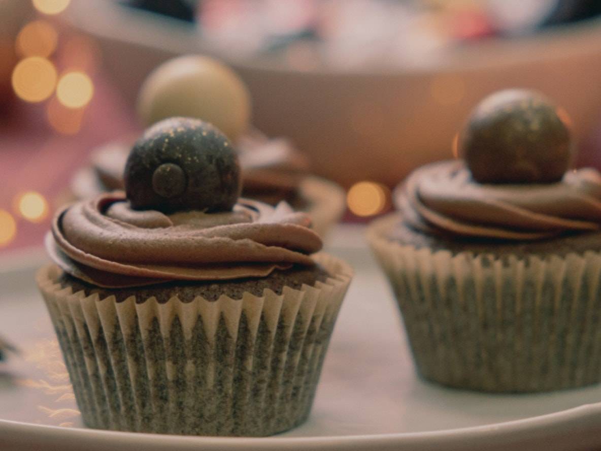 Zwei Schokoladen-Cupcakes mit Zuckerguss und Schokoladenkugeln, auf einem Teller.