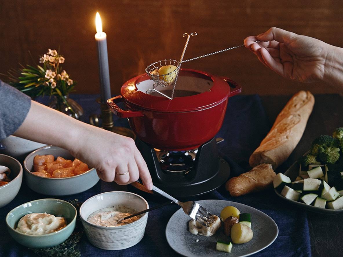 Ein Fondue-Topf mit verschiedenen Zutaten und Saucen, bei Kerzenlicht.