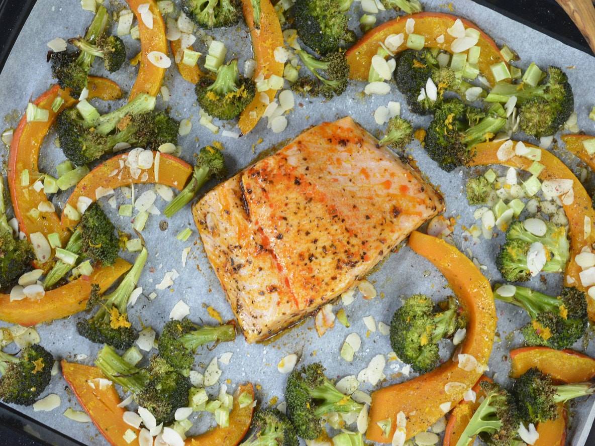 Gebratener Lachs mit Brokkoli, Kürbis und Mandelsplittern auf einem Backblech.