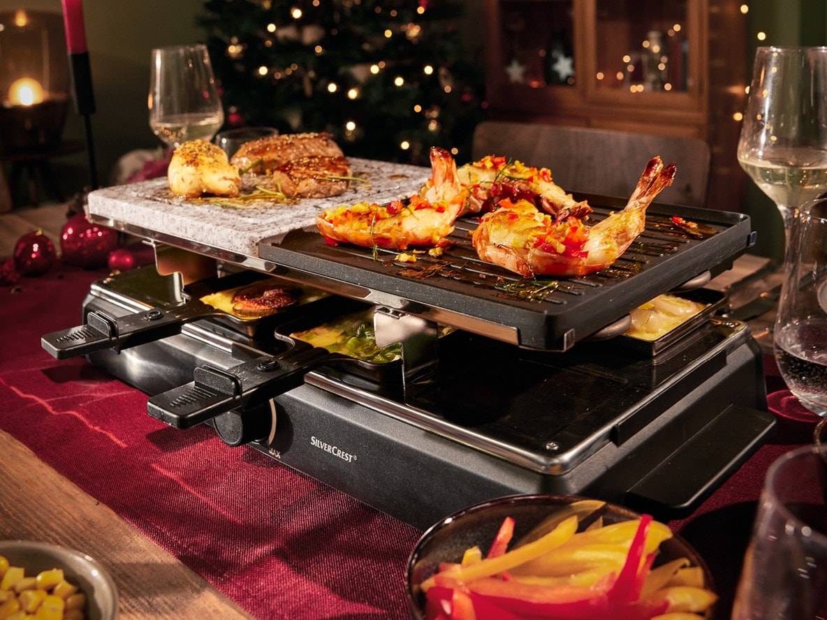 SilverCrest Raclette-Grill mit Stein- und Grillplatten, Garnelen und Fleisch zu Weihnachten zubereitend.
