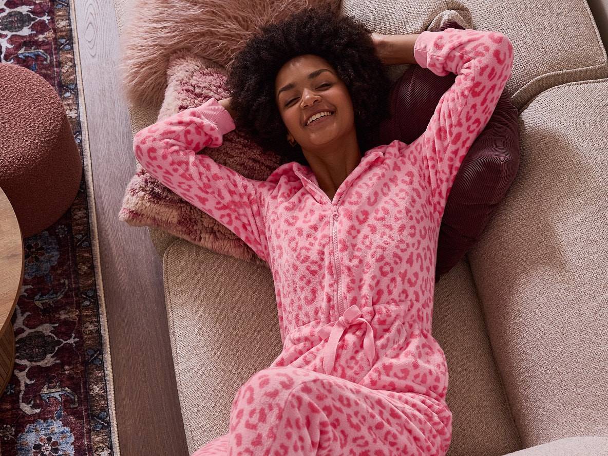 Lächelnde Frau in einem rosa Leoparden-Schlafanzug, die auf einem Sofa liegt.